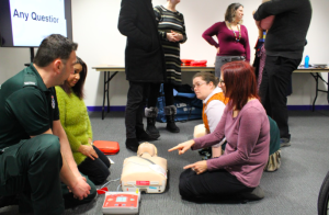 A group of attendees sat around a CPR mannequin asking questions